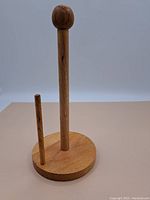 Front view of the wooden paper towel holder showing the round base, main vertical rod with knob, and shorter rod to hold the roll.