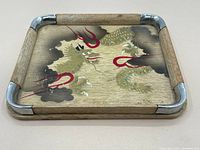 Angled top view of the small wooden tray showing the painted dragon design and metal corner accents.