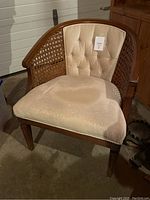 Front view of beige upholstered armchair with oak wood frame and rattan weave sides, showing tufted backrest and cushioned seat with stain.