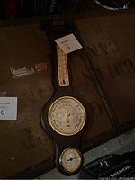 Full view of the wood and brass barometer set on a wooden surface showing overall condition and all measurement dials.