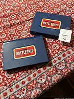 Two closed blue plastic Battleship game cases with classic logo on top