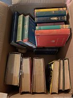 Photo showing the tops and spines of several classic hardcover books packed in a cardboard box, titles visible include several known classics.