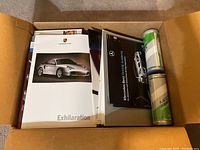 Box with various car brochures visible including Porsche Exhilaration cover and a Mercedes-Benz brochure