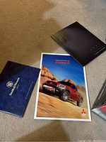 Mitsubishi Raider brochure with pickup truck on cover next to a black folder with embossed text