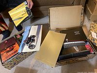 Two open cardboard boxes filled with various car brochures including 1971 Buick Riviera and other GM models