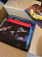 Open box showing a 2001 Chevrolet Camaro brochure on top of a pile of assorted car brochures.