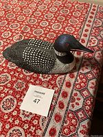 Top view of carved wooden loon bird on patterned tablecloth.