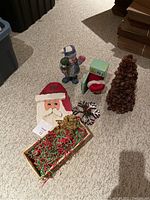 Full set of six assorted Christmas decor items laid out on carpet including carved Santa plaque, figurines, pinecone tree, and decorative box.