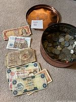 Copper tin with lid on carpet, scattered international banknotes beside it