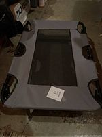 Top-down view of elevated dog bed showing the gray fabric and mesh center with black metal frame and corner joints.