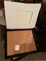 Two black plastic frames laid flat on a surface, showing the backside with cardboard backing and transparent protective covers.