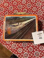 Top view showing CN train image and plastic handle on vintage metal lunch box with orange border.