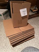 Stack of flat-packed, unused brown square cardboard boxes approximately 6.5 inches per side.