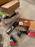 Collection of tape dispensers, packing materials, and stationery items on carpeted floor.