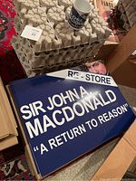 Replica lawn sign for Sir John A Macdonald with white text on blue background 'A Return to Reason' phrase.