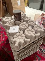 Stacked trays holding 46 new lawn signs made of rigid molded pulp, with one ceramic mug placed on top showing Canadian flag and historical design.