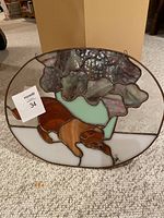 Photo showing the stained glass panel lying flat, highlighting the dog under a tree design with various colors of glass.