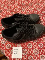 Pair of black steel toe work shoes on a patterned red tablecloth, size 12 indicated by a card.