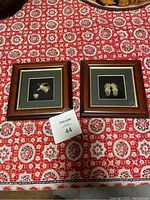 Two framed pieces of Middle Eastern silver miniatures sitting on a red patterned fabric surface.