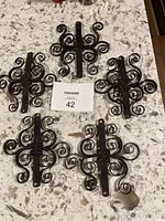 Five small identical wrought iron wall decor pieces laid out on a counter, showing full set.