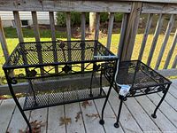 Photo showing both black wrought iron outdoor tables, one rectangular with lower shelf and one square.