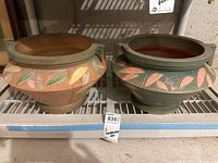 Front view of two heavy hand-painted pots with leaf motifs on a metal shelf showing colors and details of each pot.