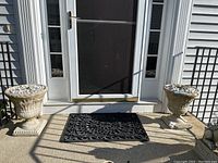 Full view of two stone planters placed outside by a door on a porch.