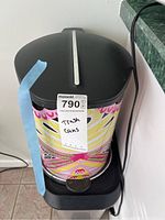 Colorful printed trash can, front view, with black lid and foot pedal, marked with lot label
