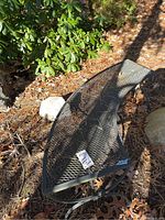 One black wrought iron bench showing the curved mesh seat and metal legs, placed outside surrounded by natural ground cover and greenery.