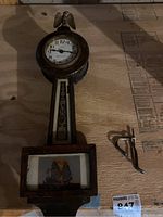 Photo showing full view of wooden antique banjo wall clock laying flat on a wooden surface with two metal keys/pieces beside it.
