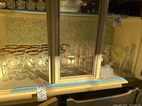 Photo of multiple sets of wine glasses in a cabinet, some with gold rims and some clear.