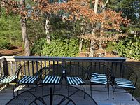 Six black wrought iron patio chairs with green and white striped cushions lined up on an outdoor patio railing, showing the full set.