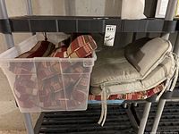 Set of multicolor striped cushions inside clear plastic tote and two beige corduroy cushions stacked beside it on shelf.