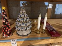 Two decorative Christmas trees and two electric candles with gold-tone holders on basement wooden shelf.