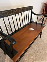 Full front three-quarter view of deacon bench showing black frame, spindled backrest and brown seat.