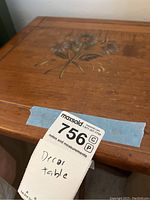 Top and edge close up of wooden side table showing floral design and wood grain, with seller sticker visible.