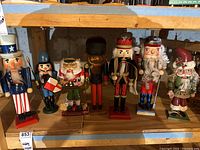 Full view of the seven assorted holiday nutcracker figurines on a shelf, showing variety in size, color, and style.