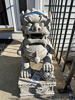 Front view of the gray stone lion sculpture outdoors on a concrete surface near railing.