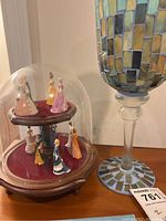 Photo showing a wooden two-tiered round display stand lined with red fabric holding 12 porcelain ladies figurines in vintage dresses under a glass dome, alongside a mosaic patterned glass vase with a tall stem.