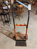 Front view of the orange and black push dolly showing the handle, platform, and wheels.