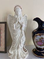White ceramic angel figurine with gold accents and praying hands