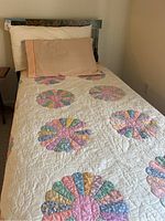 Full view of the twin bed made up with patchwork quilt and pillows showing fabric details and sage green bed frame.