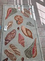 Full view of the rectangular seashell patterned rug on a tile floor, showing the various seashell designs and overall color scheme.