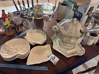 Overview of the serving punch bowl with ladle and four white ceramic shell-shaped serving plates on wooden table with other household items in background.