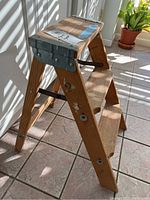 Side view of the wooden step stool showing two wide steps, foldable structure, and metal reinforcements at the top and sides.