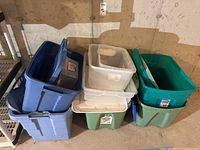 Plastic storage totes stacked against a wall, showing multiple colors and sizes