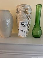 Three vases displayed on a shelf: a white Lenox vase, a white ceramic decorative vase with open lattice design, and a green glass vase