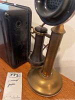 Close-up photo of the brass base, stem, and black receiver of the vintage candlestick phone alongside the black bell box.