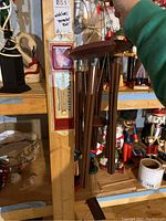 Photo of bronze metal wind chimes with wooden top and bottom hanging indoors on a wooden beam near a thermostat reader.