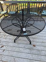 Full view of the outdoor black wrought iron round table with mesh top, showing tripod legs and umbrella hole.